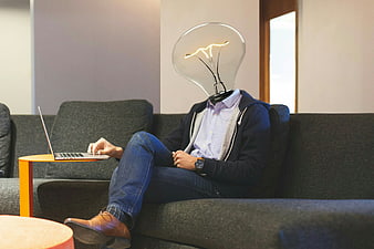 Man with lightbulb head working on laptop on couch