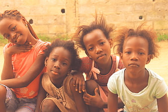 Four African girls sitting together outdoors against a stone wall