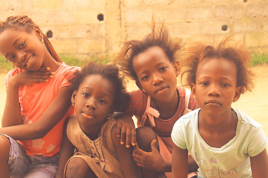 Four African girls sitting together outdoors against a stone wall