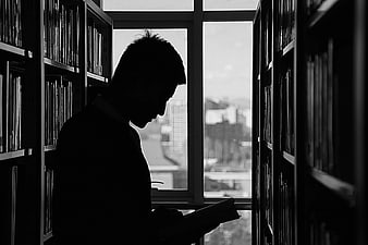 Silhouette of man reading book in library aisle