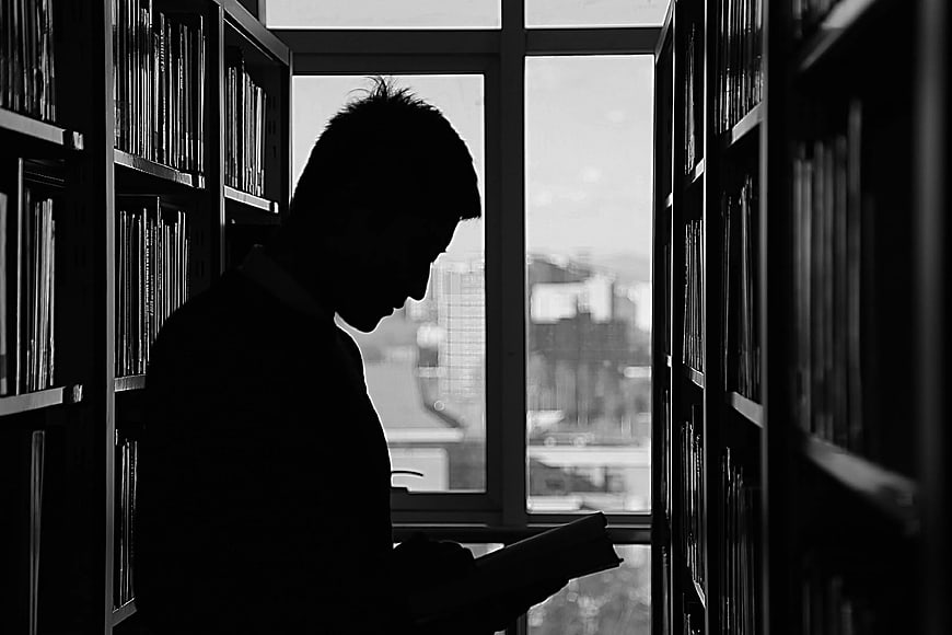 Silhouette of man reading book in library aisle