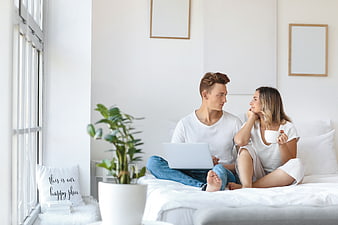 Young couple relaxing on bed with laptop and coffee