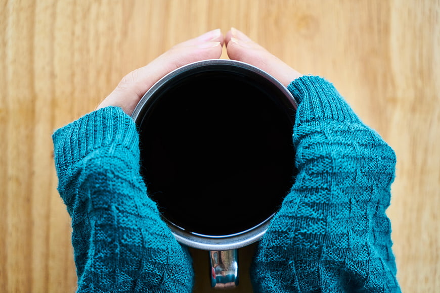 Hands holding black coffee mug in teal sweater