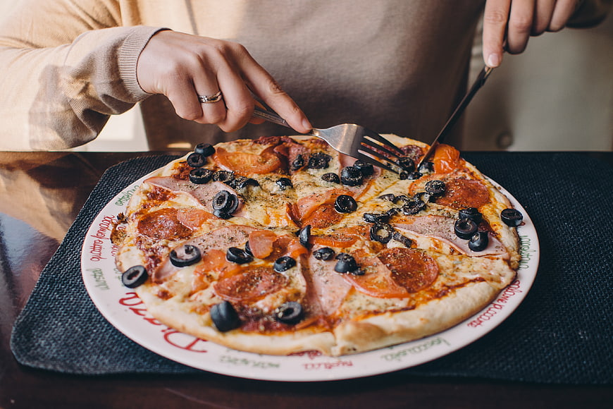 Person Cutting Pepperoni and Olive Pizza with Fork and Knife