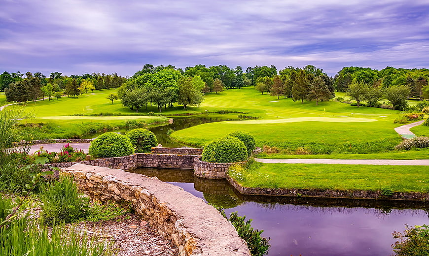 Lush green golf course with stone bridge and water hazard