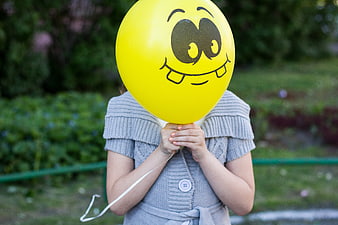 Child holding yellow smiley face balloon in park