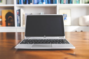 Silver Acer Laptop on Wooden Desk with Blurred Bookshelf Background
