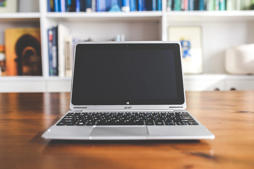 Silver Acer Laptop on Wooden Desk with Blurred Bookshelf Background