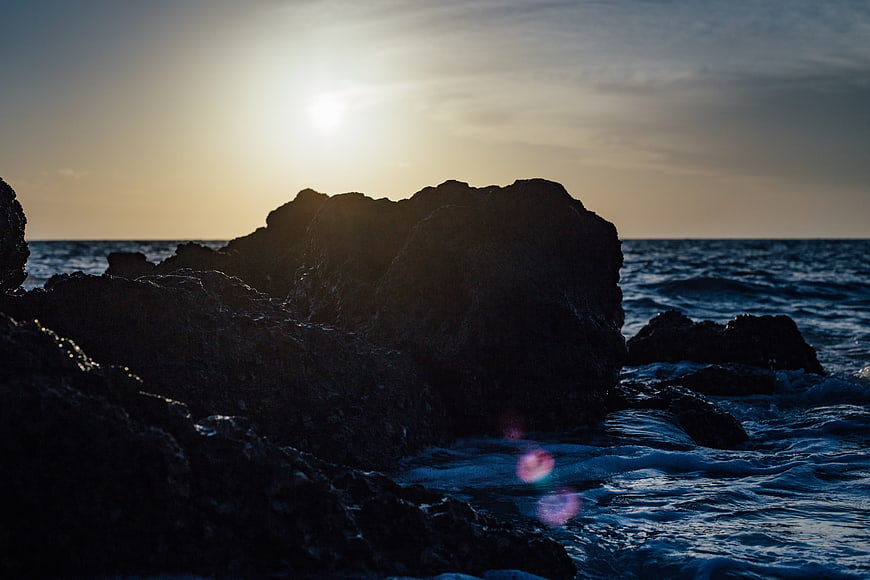 Silhouette of dark rocks against ocean sunset waves