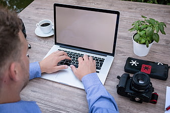 Man Typing on Laptop Beside DSLR Camera and Coffee
