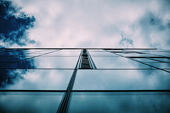 Low angle view of modern glass skyscraper reflecting cloudy sky