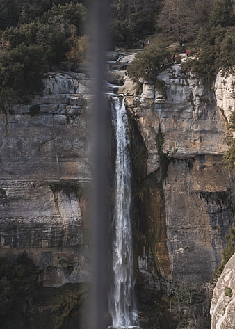 Tall waterfall cascading down rocky cliff with hikers
