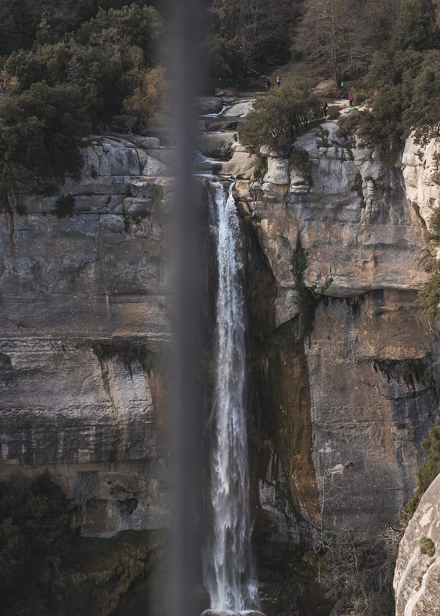 Tall waterfall cascading down rocky cliff with hikers