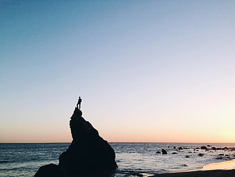 Silhouette of Man Standing on Rock at Sunset Beach