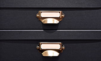Close-up of vintage brass drawer pulls on black textured cabinet