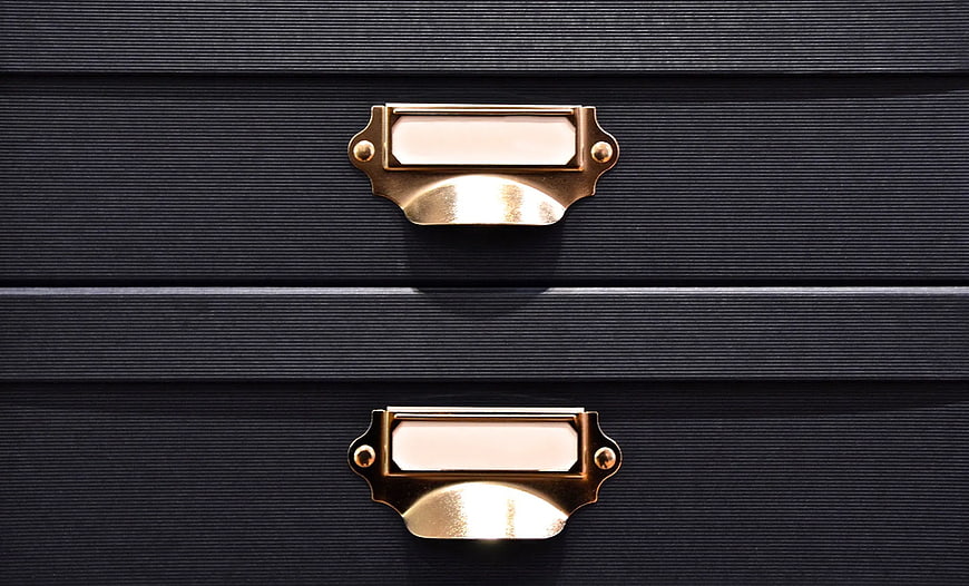 Close-up of vintage brass drawer pulls on black textured cabinet