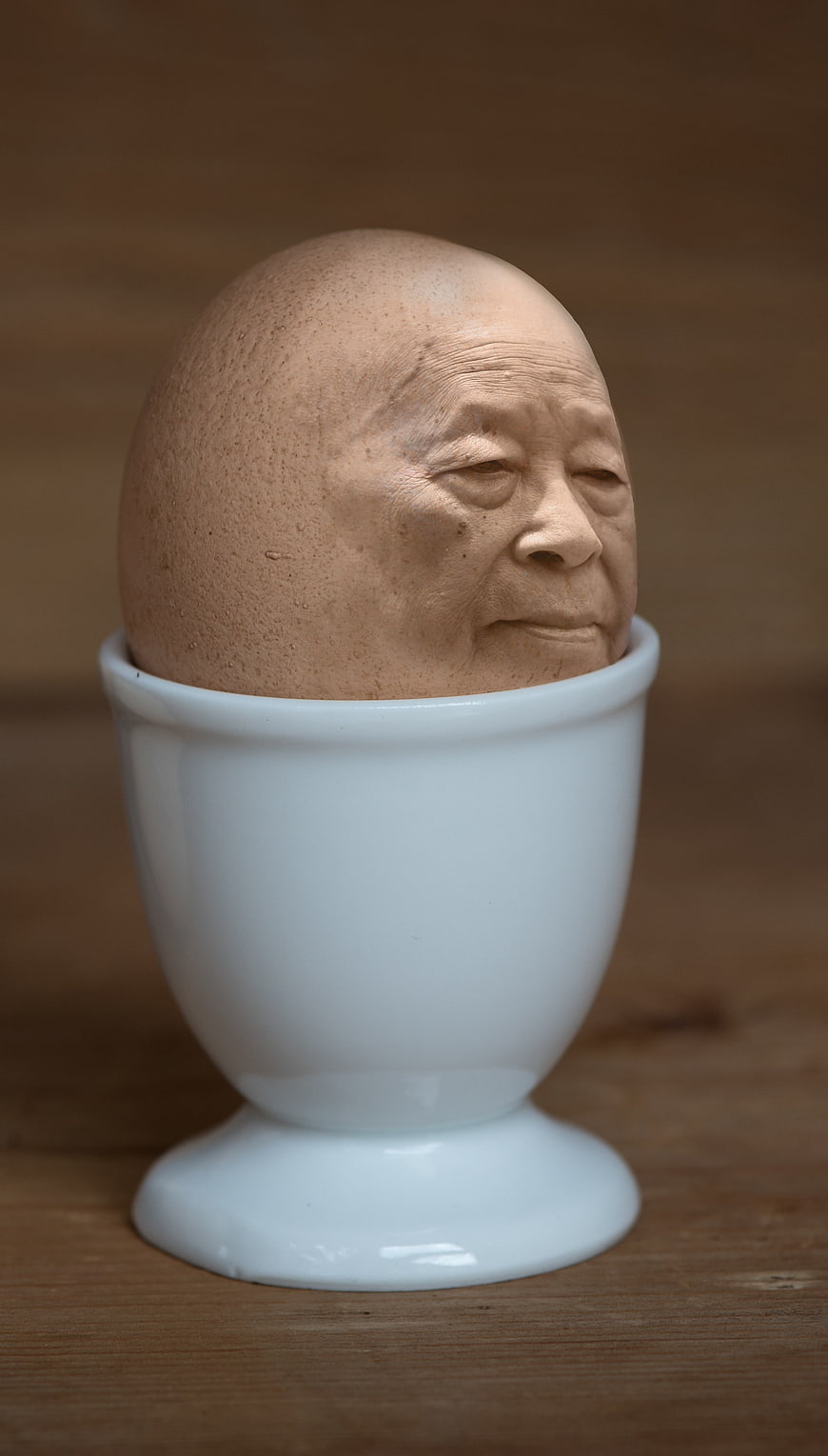 Surreal egg with elderly face in white egg cup
