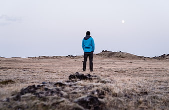 Man in Blue Jacket Standing Alone in Vast Highland Landscape