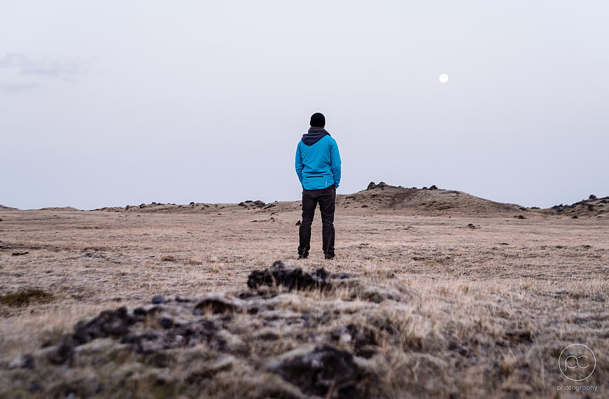 Man in Blue Jacket Standing Alone in Vast Highland Landscape