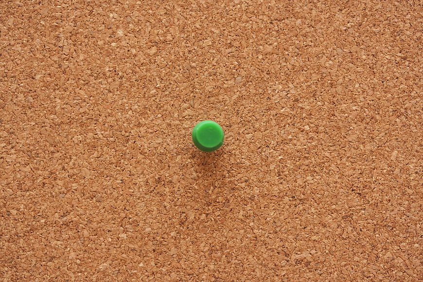 Green Push Pin on Textured Cork Board Background