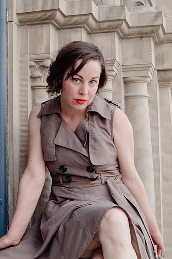 Woman in beige trench coat dress sitting against stone architecture