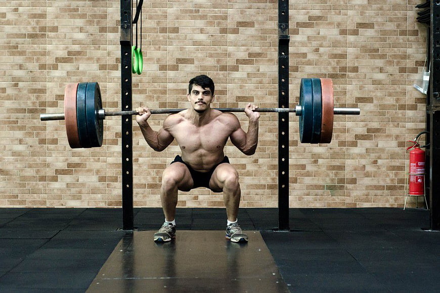 Shirtless Male Weightlifter Performing Front Squat in Gym