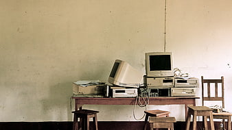 Outdated computer hardware and CRT monitors stacked on a wooden desk