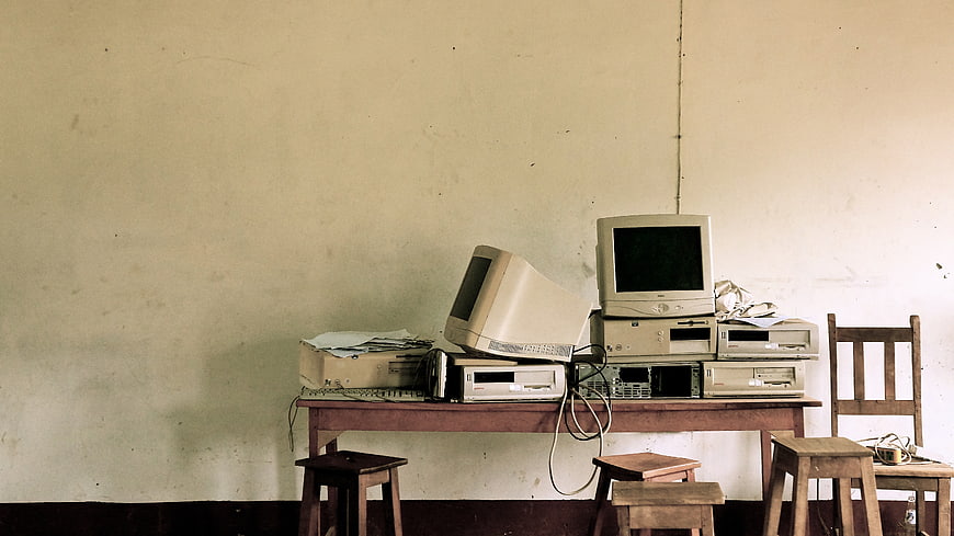 Outdated computer hardware and CRT monitors stacked on a wooden desk