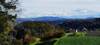 Panoramic autumn landscape with snow-capped Alps and rolling green hills
