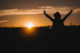 Silhouette of Woman with Arms Raised at Sunset