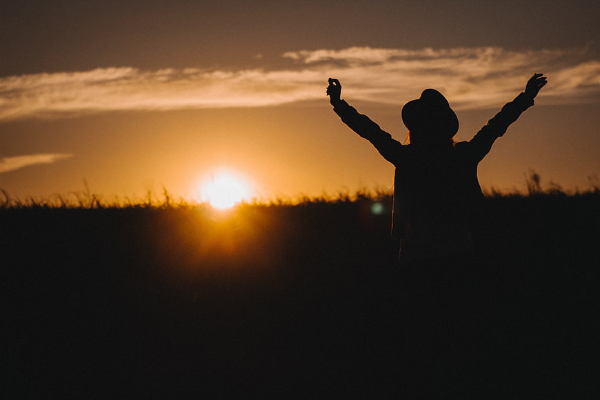 Silhouette of Woman with Arms Raised at Sunset