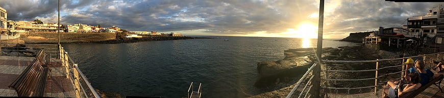 Panoramic sunset view of coastal town harbor with people relaxing