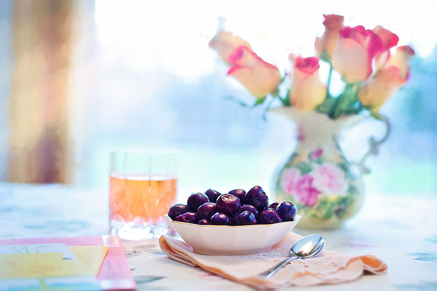 Bowl of dark cherries with roses and tea on a table