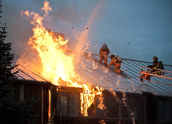 Firefighters battling intense house fire on metal roof at dusk