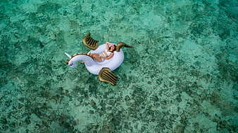 Aerial view of woman relaxing on inflatable unicorn float in turquoise ocean