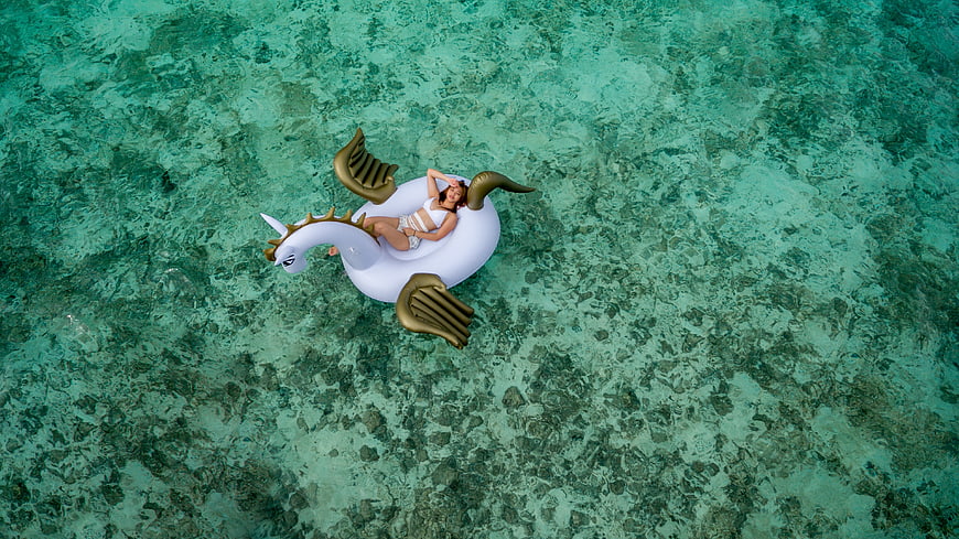 Aerial view of woman relaxing on inflatable unicorn float in turquoise ocean