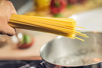 Hand holding raw spaghetti over boiling water pot