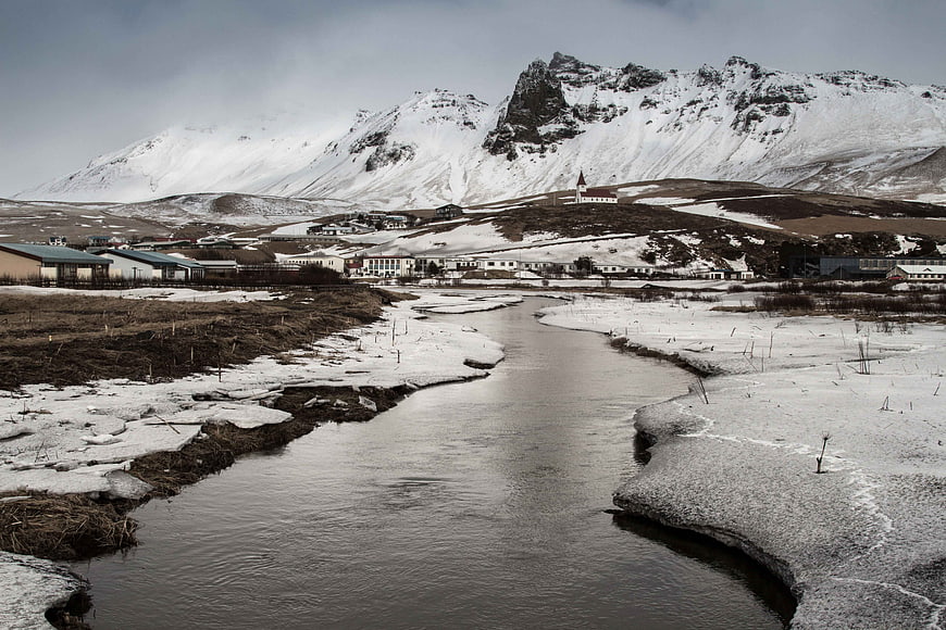 Snowy River Flowing Through Icelandic Village with Mountains