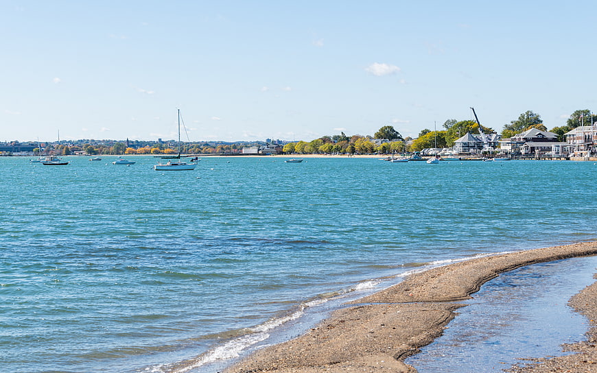 Sandy Beach Shoreline with Boats in Harbor on Sunny Day