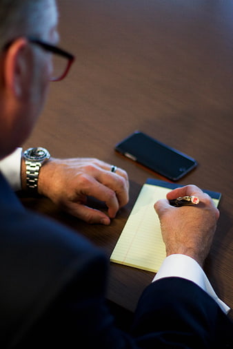 Businessman Writing Notes on Desk with Smartphone