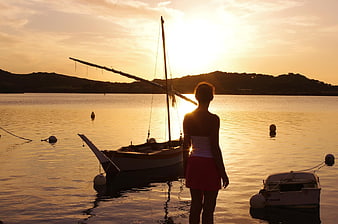 Silhouette of Woman Watching Sunset Over Harbor with Sailboat