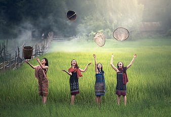 Four women in traditional dress tossing baskets in a green rice field