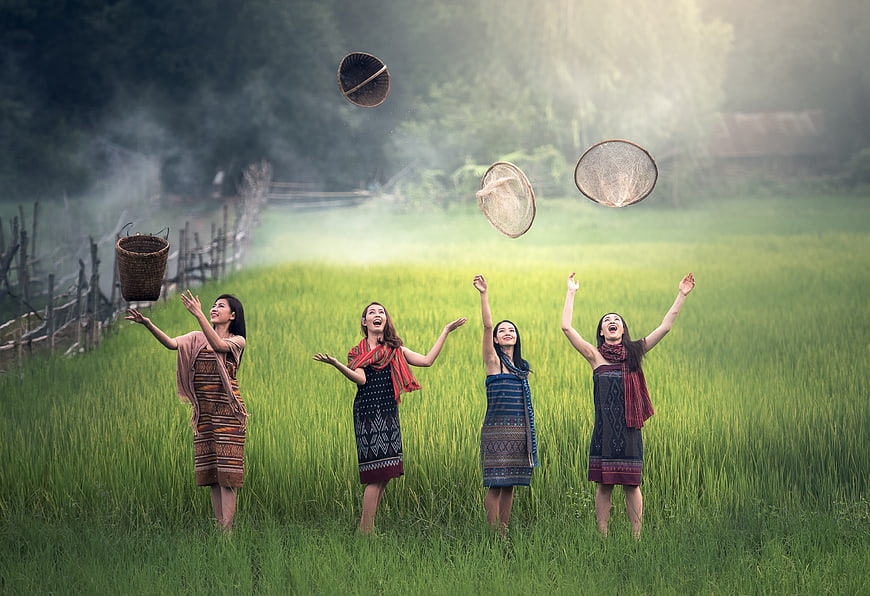 Four women in traditional dress tossing baskets in a green rice field