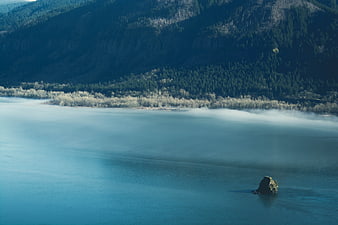 Misty Lake with Rock and Forested Mountain Background