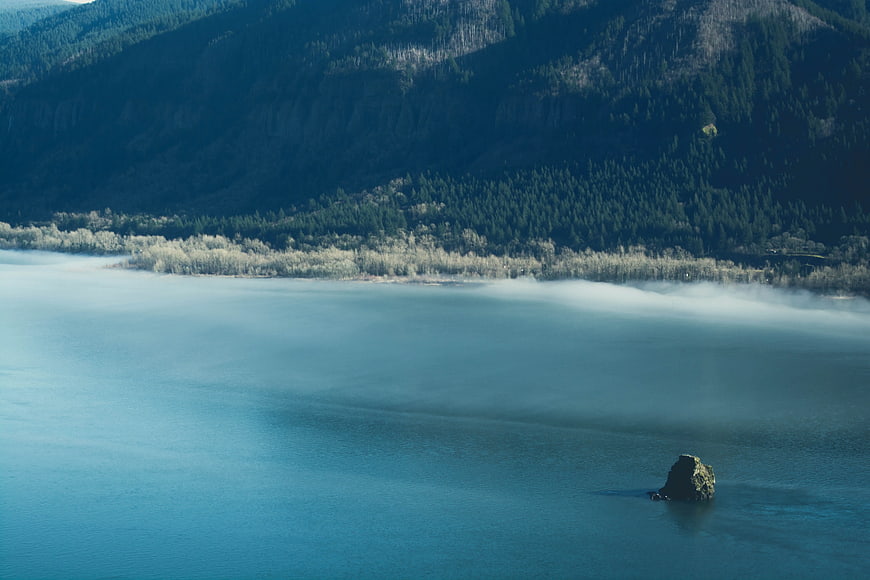Misty Lake with Rock and Forested Mountain Background