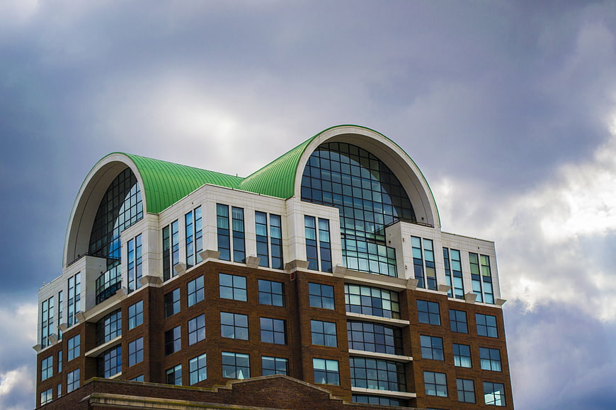 Modern office building with green arched roof against cloudy sky