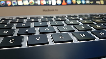 Close-up of a MacBook Pro keyboard with blurred screen background