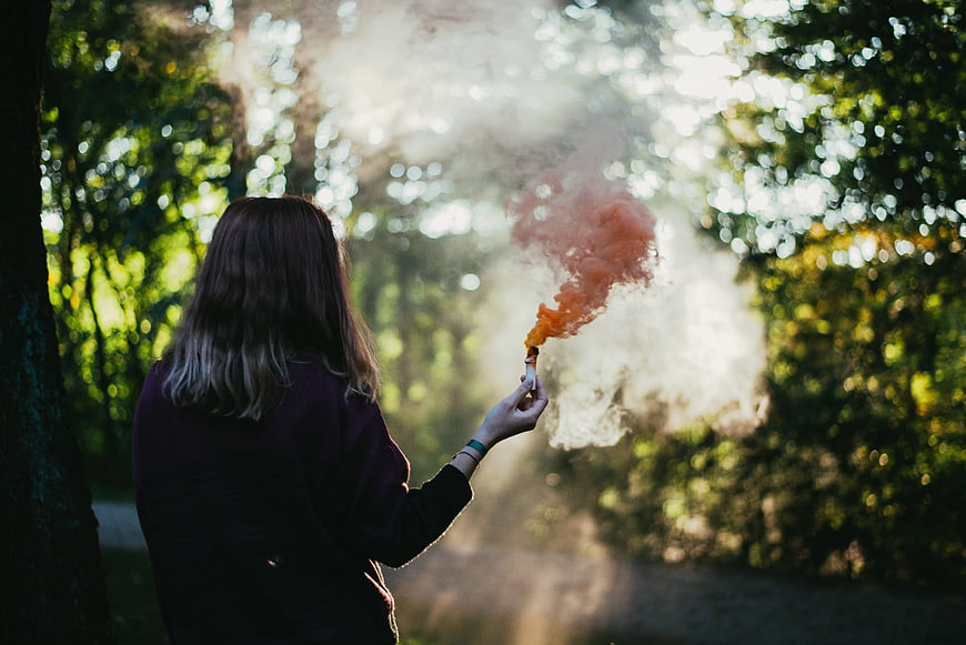 Woman Holding Orange Smoke Bomb in Forest