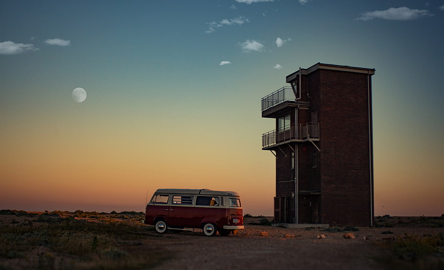 Vintage red van parked near brick tower at sunset