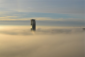 Skyscraper emerging from thick fog in a city at sunrise